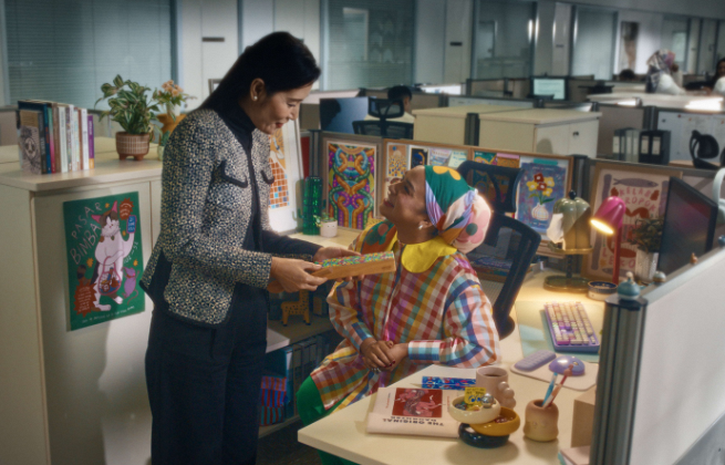 Office worker seated at desk decorated with local artworks engaged in conversation with her boss