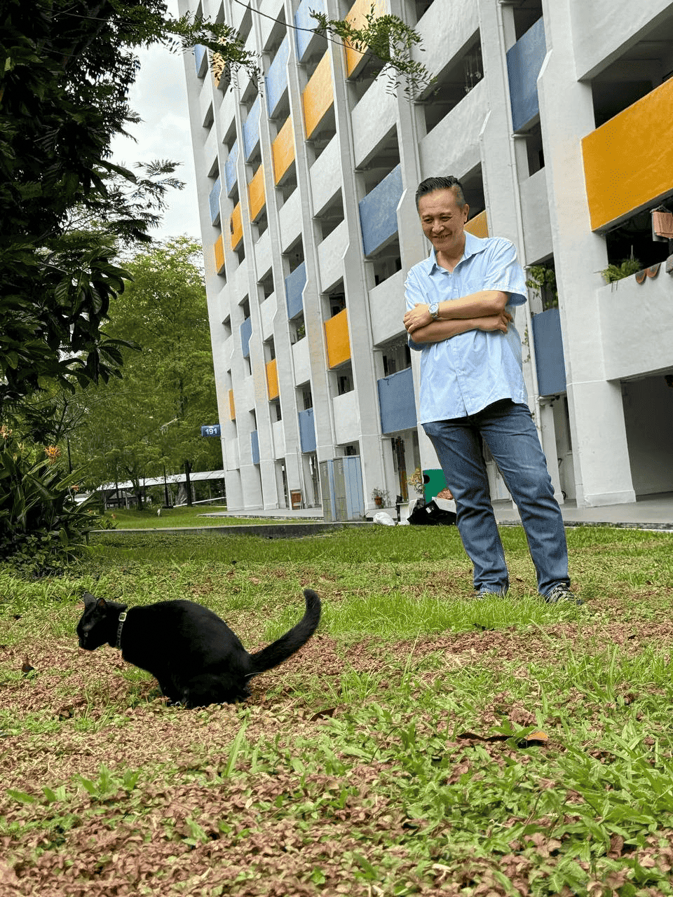Clarence Ho smiling to a black cat in the neighbourhood