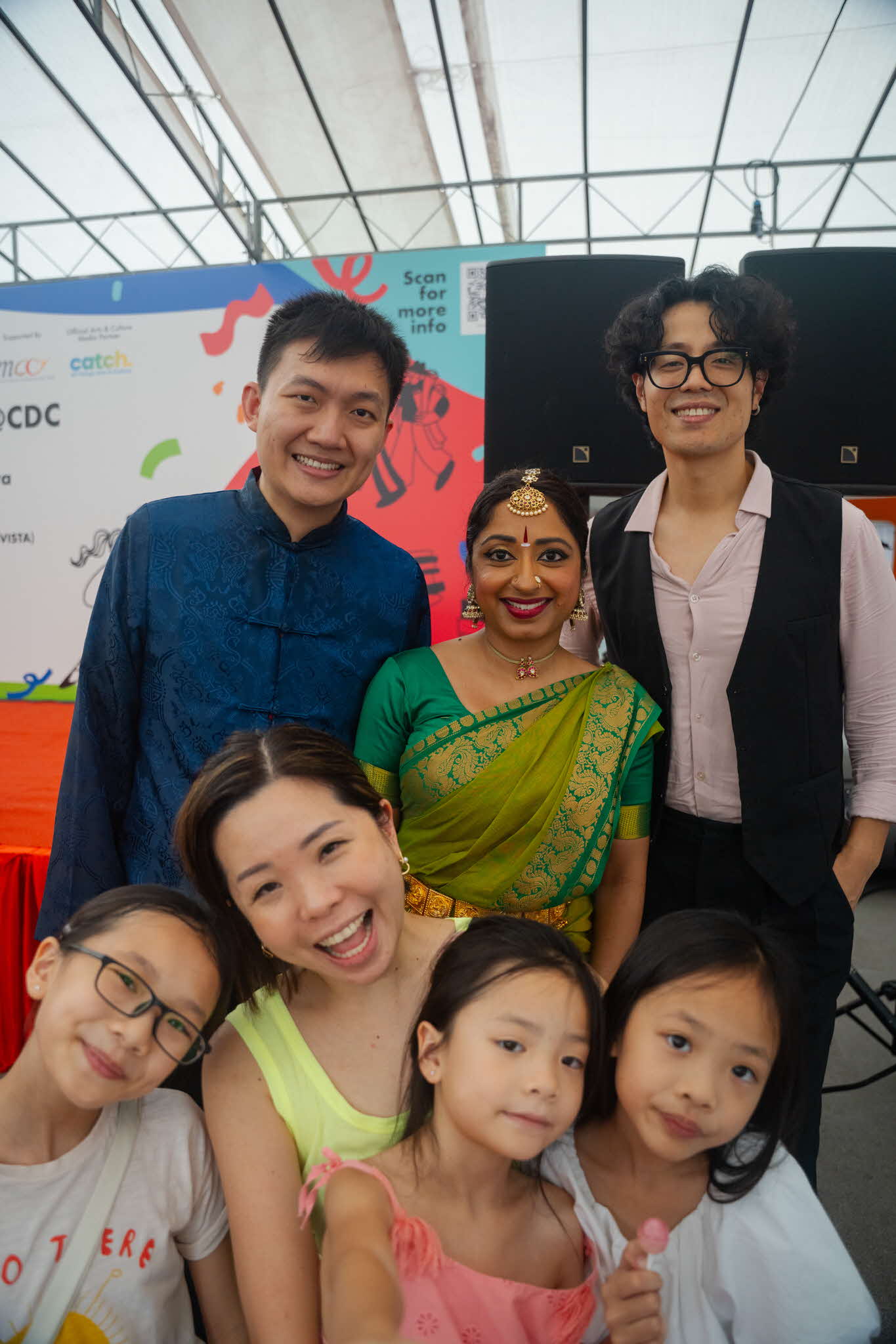 Creating memories and snapping selfies with yIN Harmony performers at ArtsEverywhere@CDC. A smiling group selfie consisting of a family of four (one parent, three children) in the foreground and three performers in their stage costumes in the background. Discover Joy Together: ArtsEverywhere@CDC — Creating Family Memories through Art