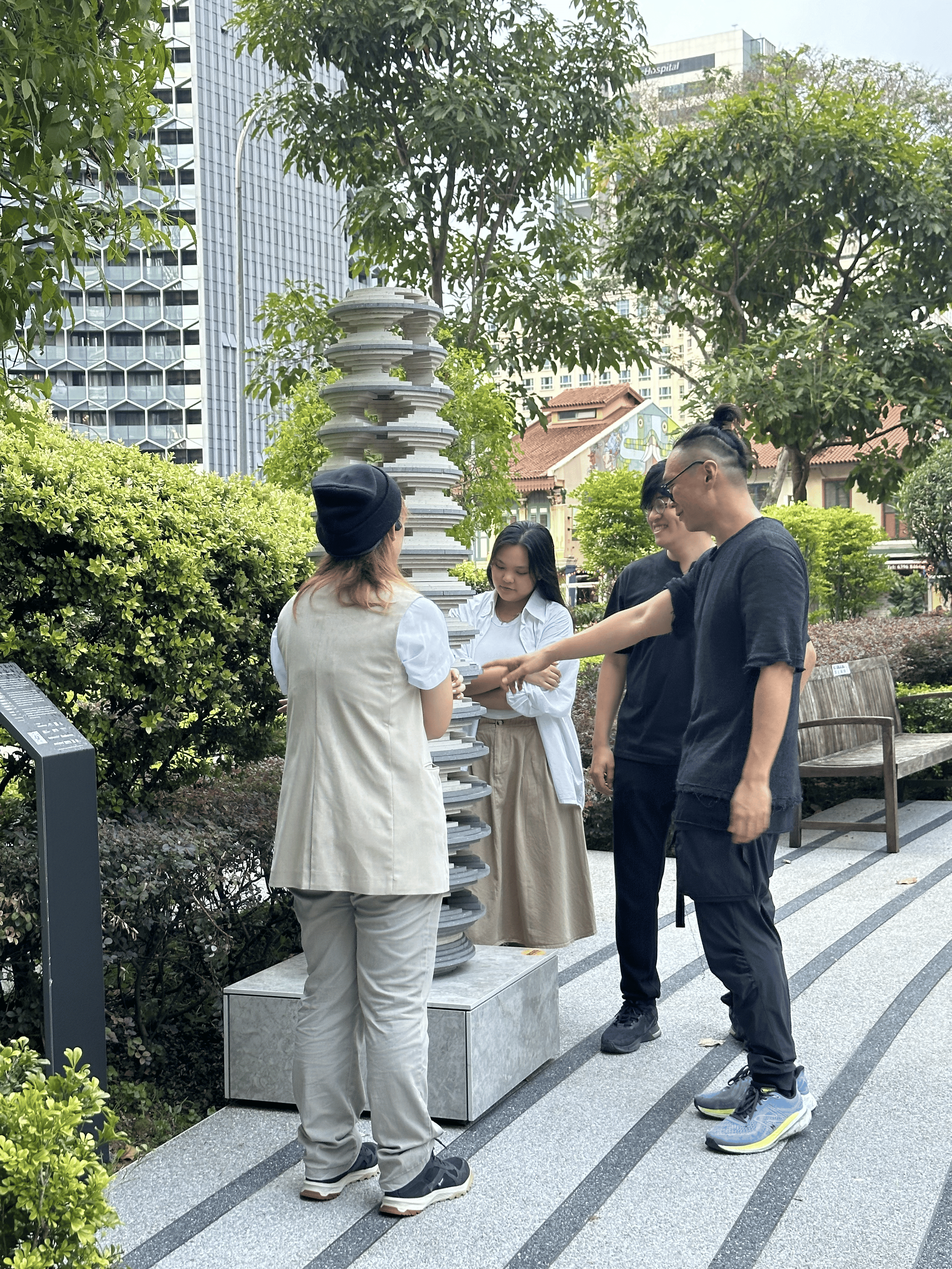 Eugene Kosgoron with fellow artists, admiring ‘Strata’ and its layers Side view of four people standing around the sculpture, admiring its layers. A man in black is pointing at the staggered surface of the disks